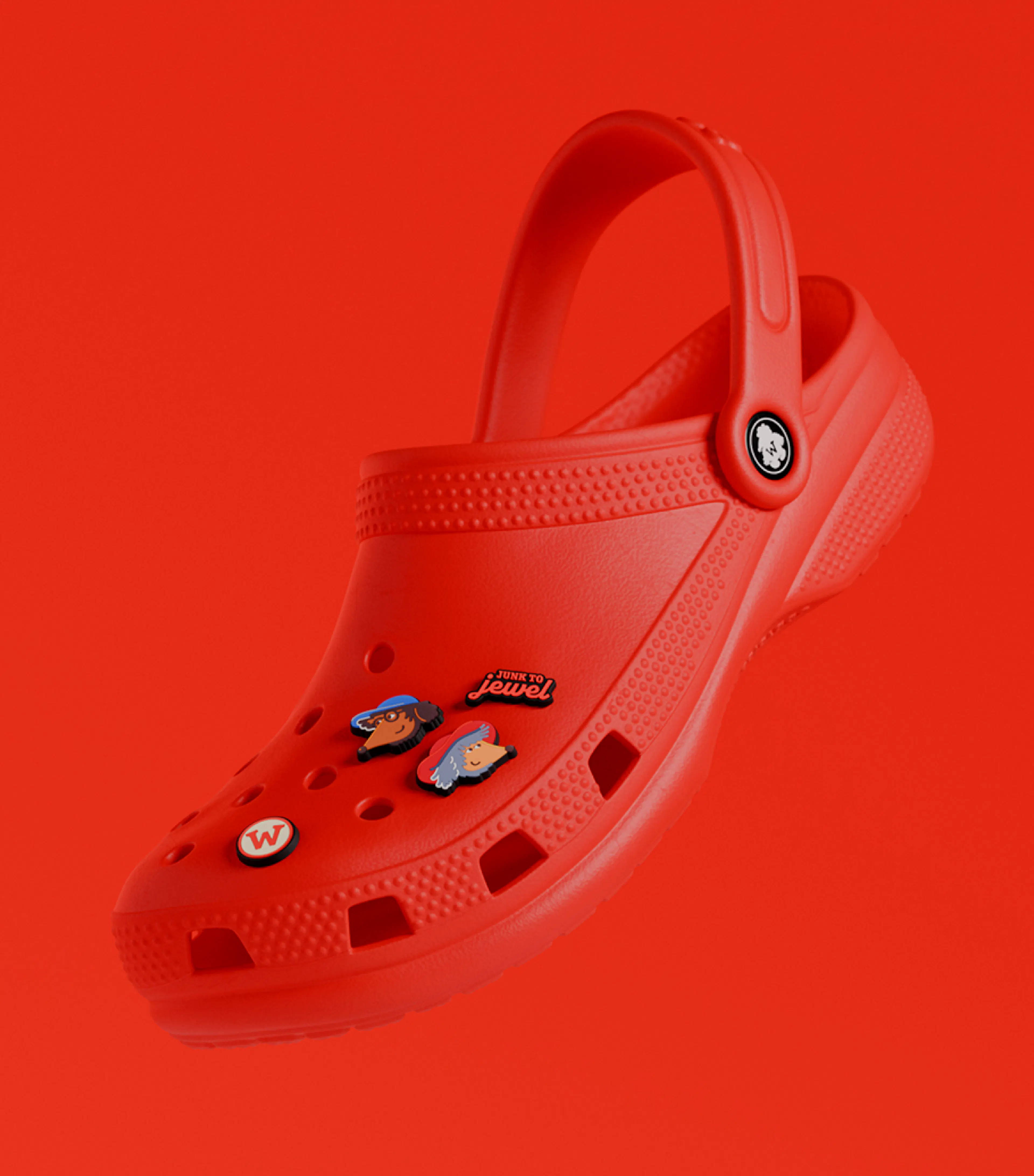A red Crocs clog decorated with Wombles charms, floating against a red background