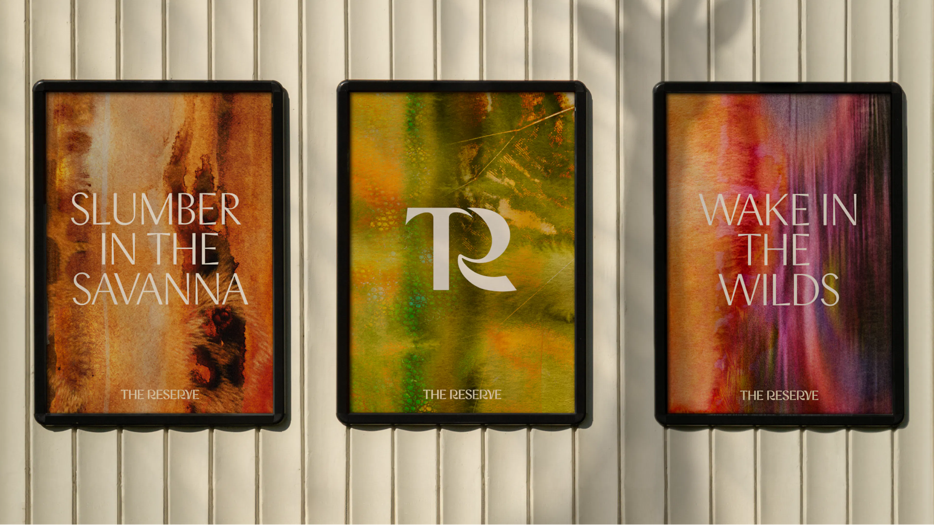 Three framed posters on a panelled wall: 'Slumber in the savanna', the TR monogram and 'Wake in the wilds', each over watercolour patterns