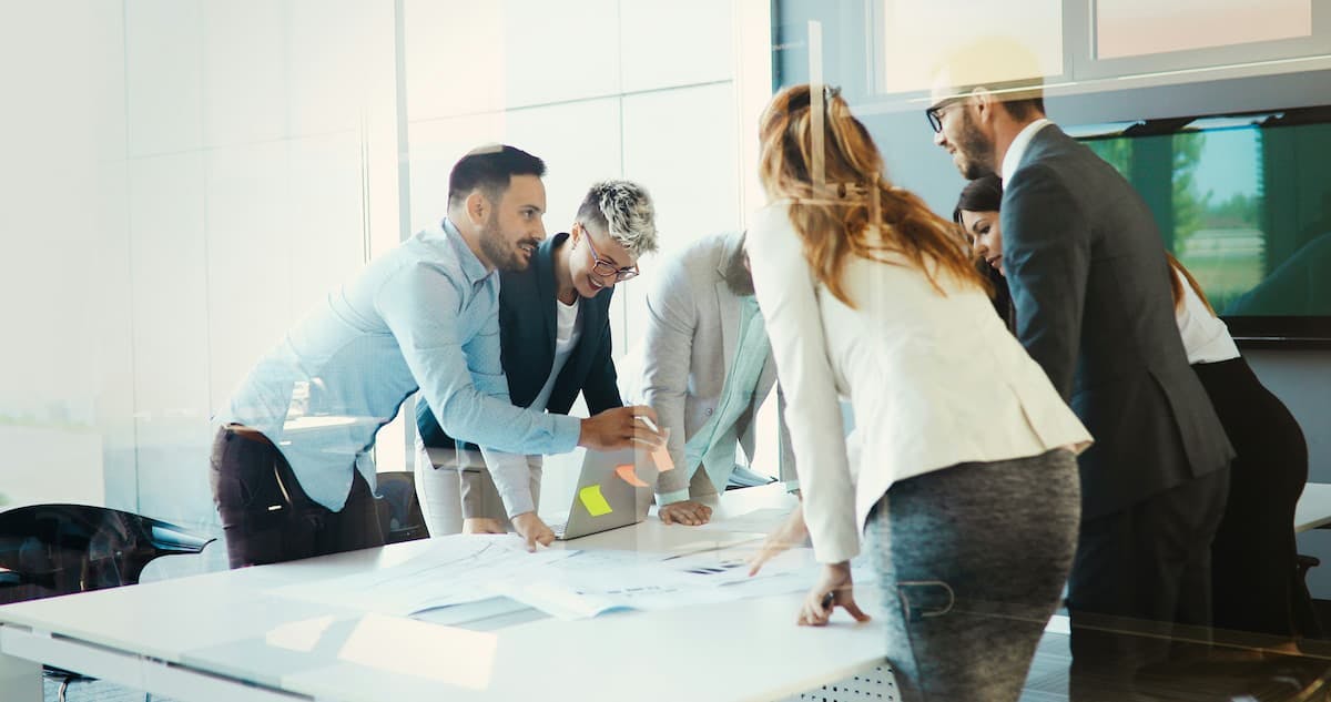A group of colleagues gathered around a table in a modern office, collaborating on documents laid out before them.