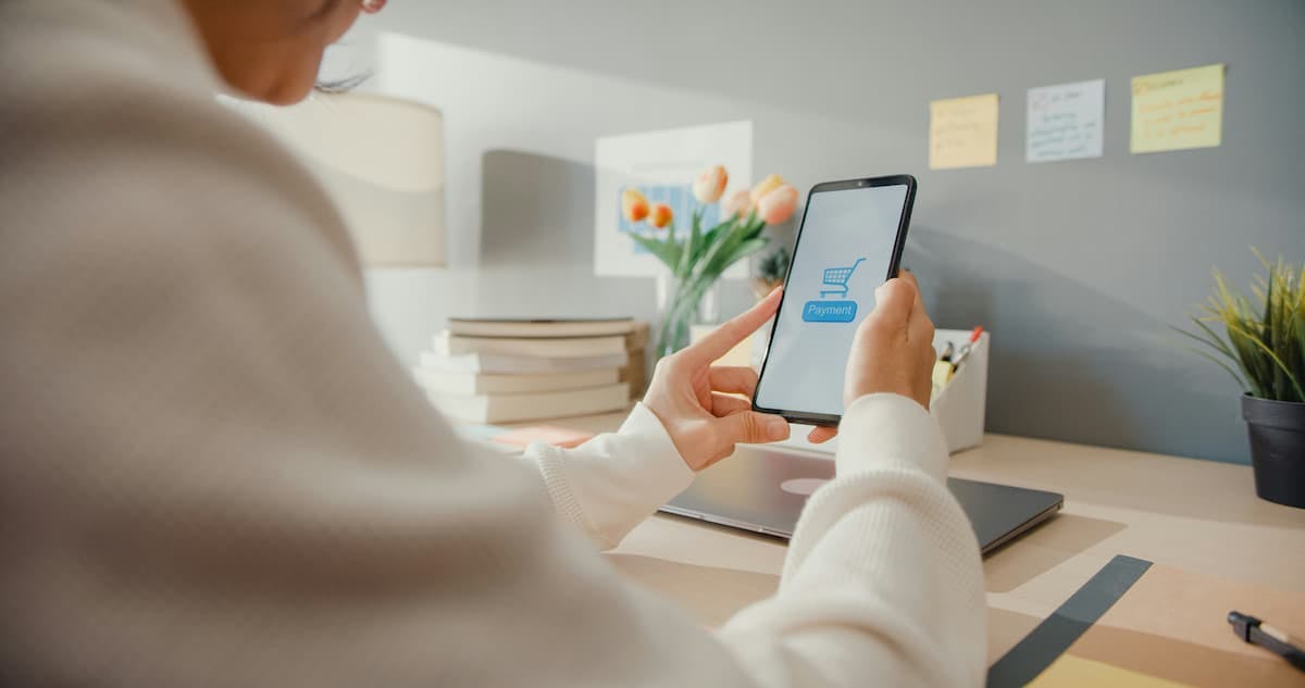 A professional workspace featuring a person holding a smartphone displaying a payment screen with a shopping cart icon and the word "Payment" visible.