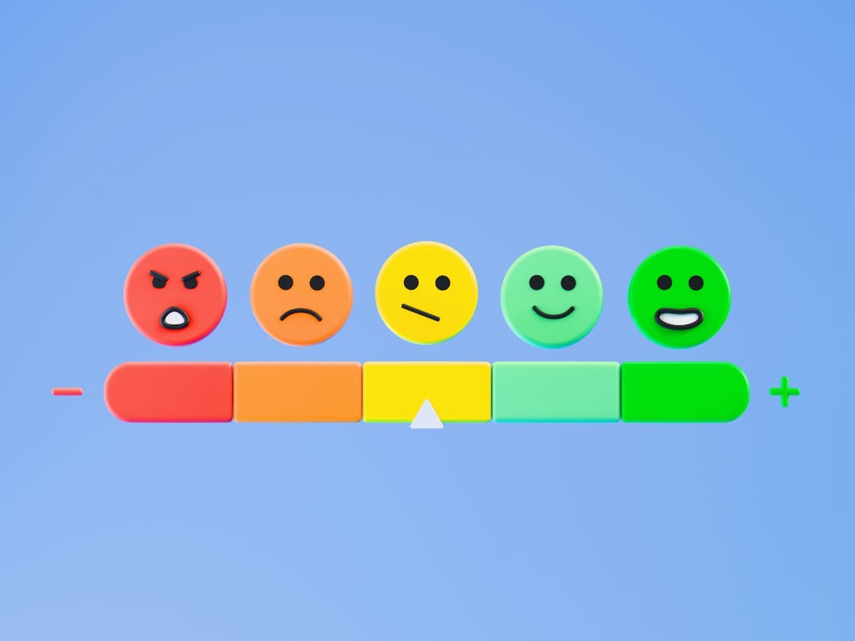 A scale depicting levels of employee satisfaction, ranging from very dissatisfied to very satisfied. It features five faces: a red angry face, an orange sad face, a yellow neutral face, a light green happy face, and a dark green very happy face. The scale is marked with a minus sign on the left and a plus sign on the right, symbolizing the spectrum of satisfaction levels.