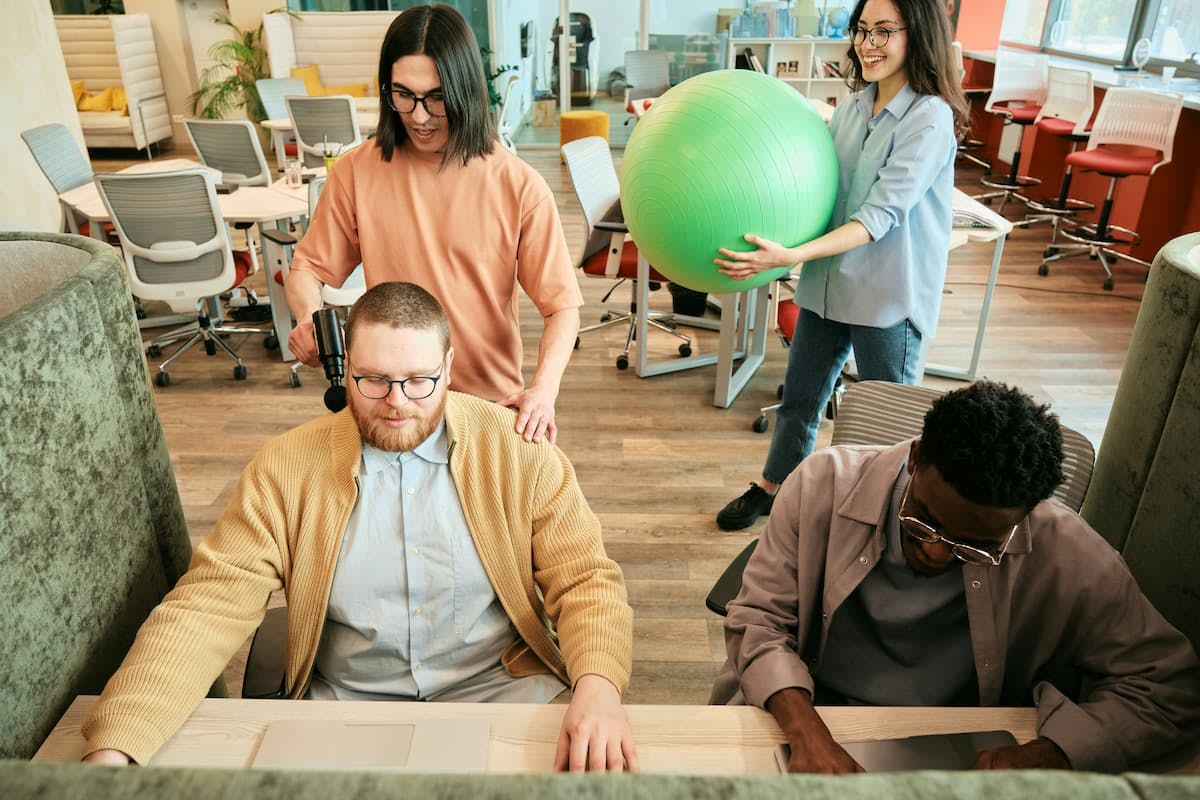 A group of people in a modern office, with one man wearing headphones and another holding a green exercise ball