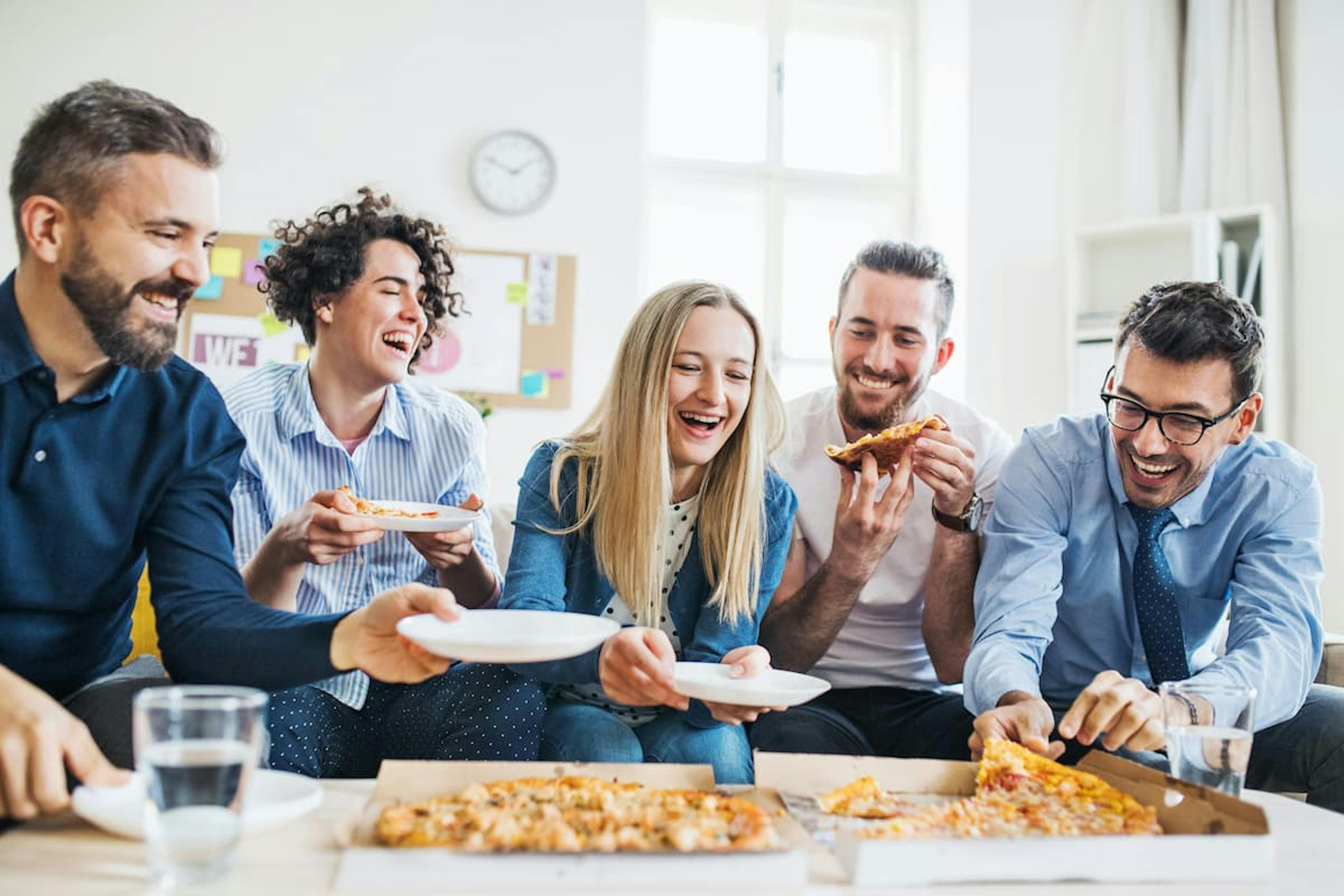 A group of friends smiling and sharing pizza in a relaxed environment, celebrating moments together