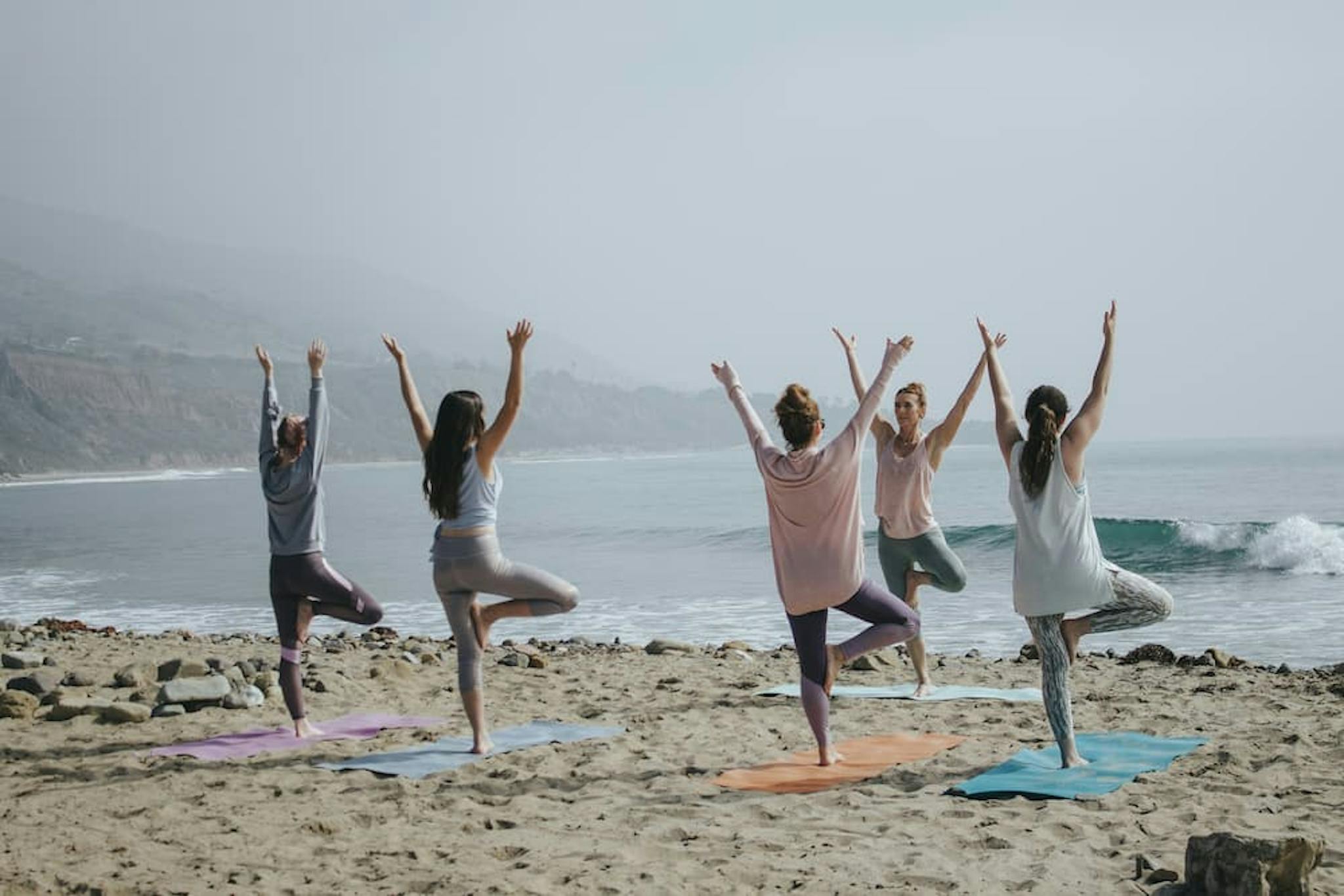 A group of women practicing yoga on the beach, performing balancing poses in harmony with nature. The scene conveys peace and connection