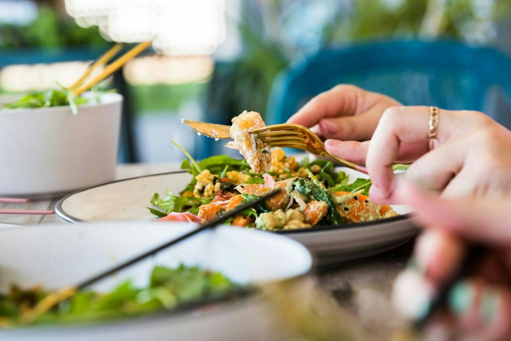 A close-up of a hand holding a fork, picking up a portion of fresh and colorful salad on a plate, with other salad dishes in the background