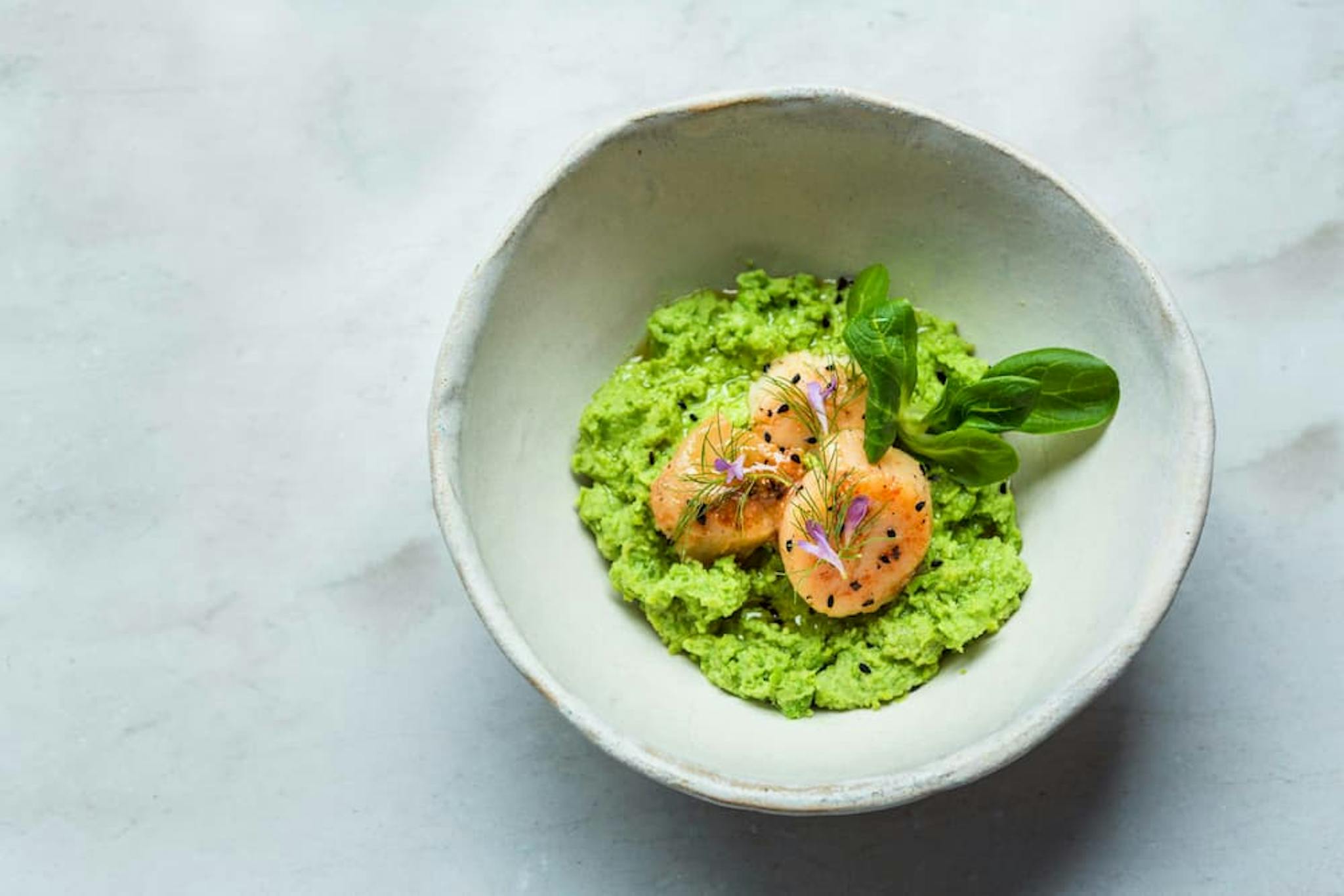 A gourmet dish featuring grilled salmon over avocado purée with touches of fresh herbs and edible flowers, in an elegant bowl