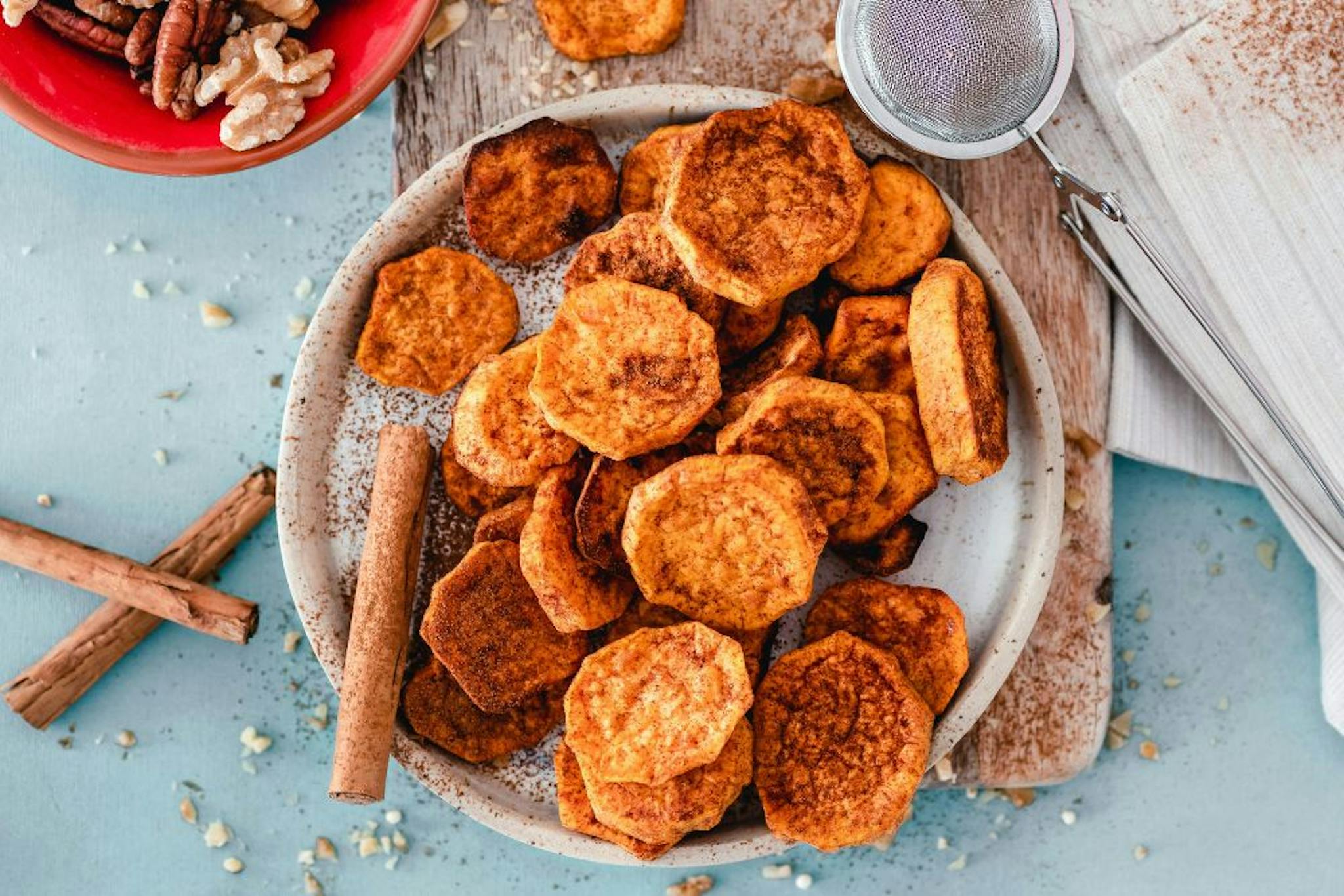 Crispy sweet potato slices served on a plate, accompanied by cinnamon and nuts