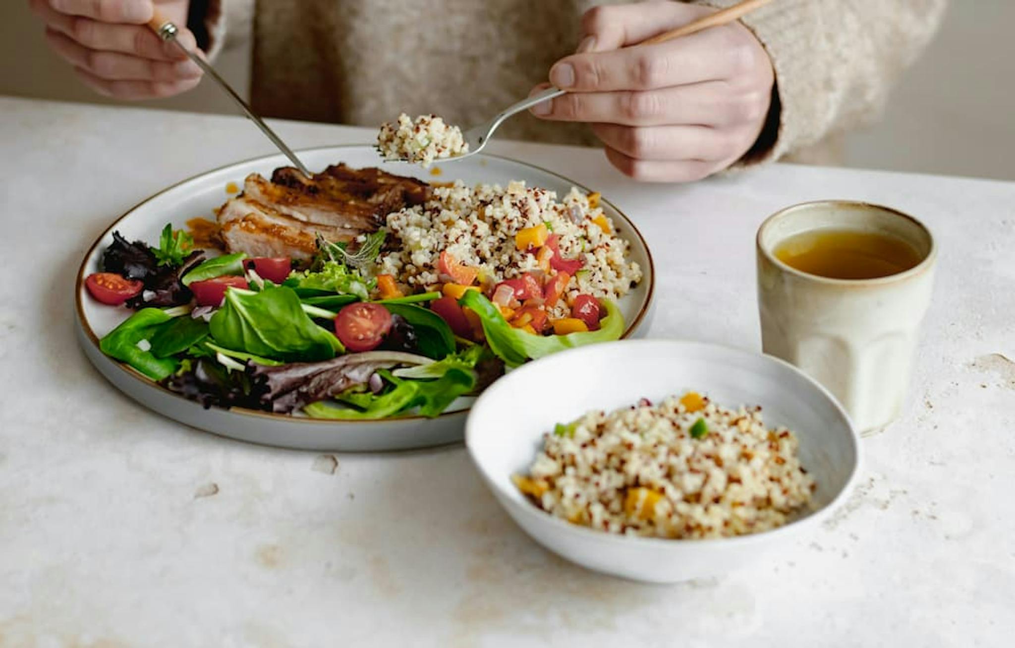 Plate with fresh salad, quinoa, grilled fillet, and a cup of tea