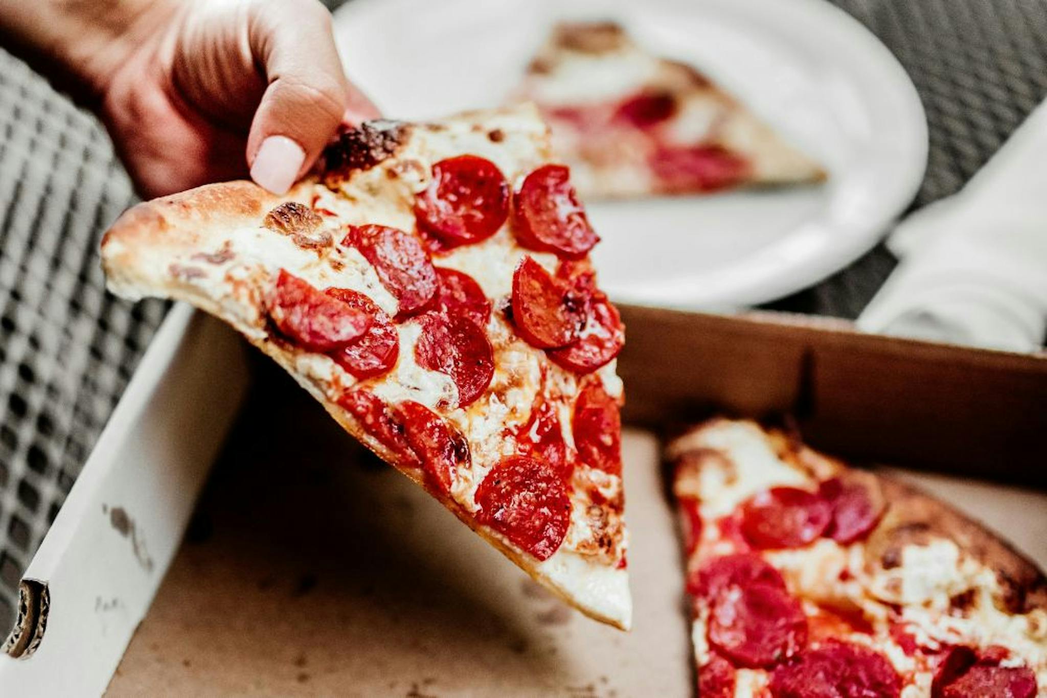 A delicious slice of pepperoni pizza being held, with the pizza box in the background