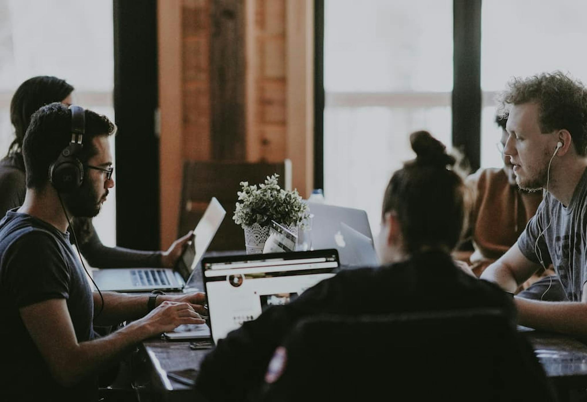 A group of people working in a collaborative environment, using laptops and headphones, focused on their team tasks.