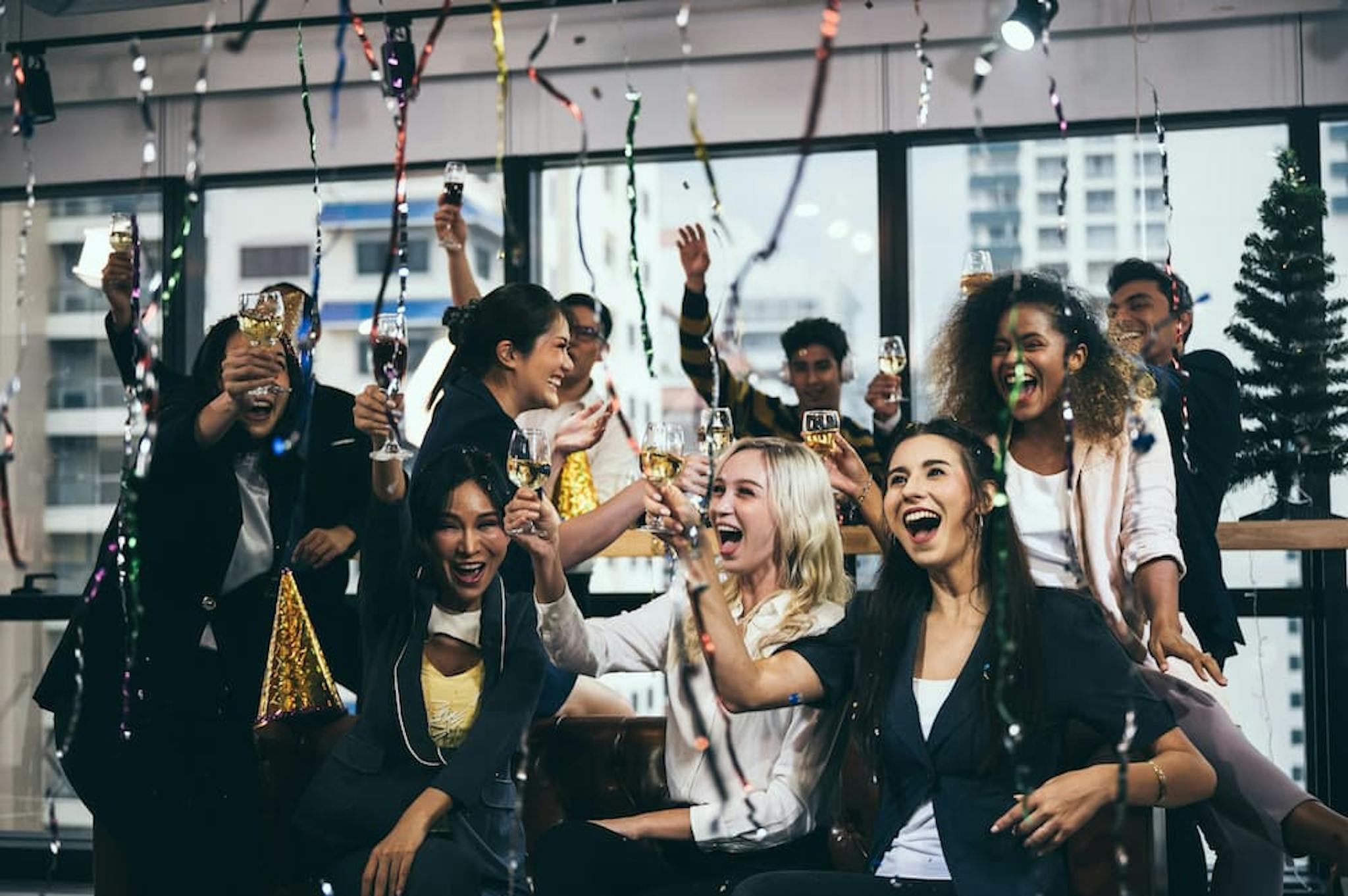 A group of excited people celebrating at a party, toasting with glasses and decorated with streamers in a festive atmosphere.