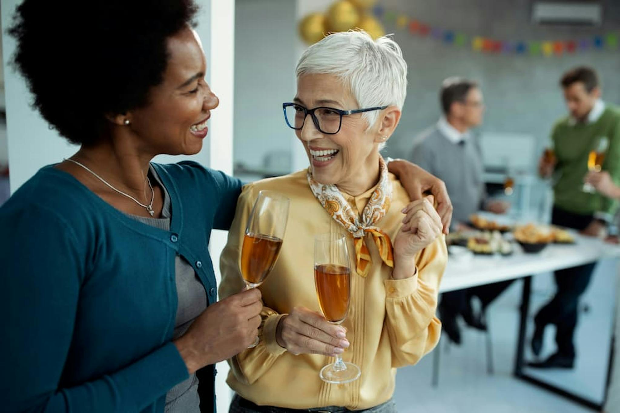 Two women smiling and toasting with glasses of drink at a social gathering