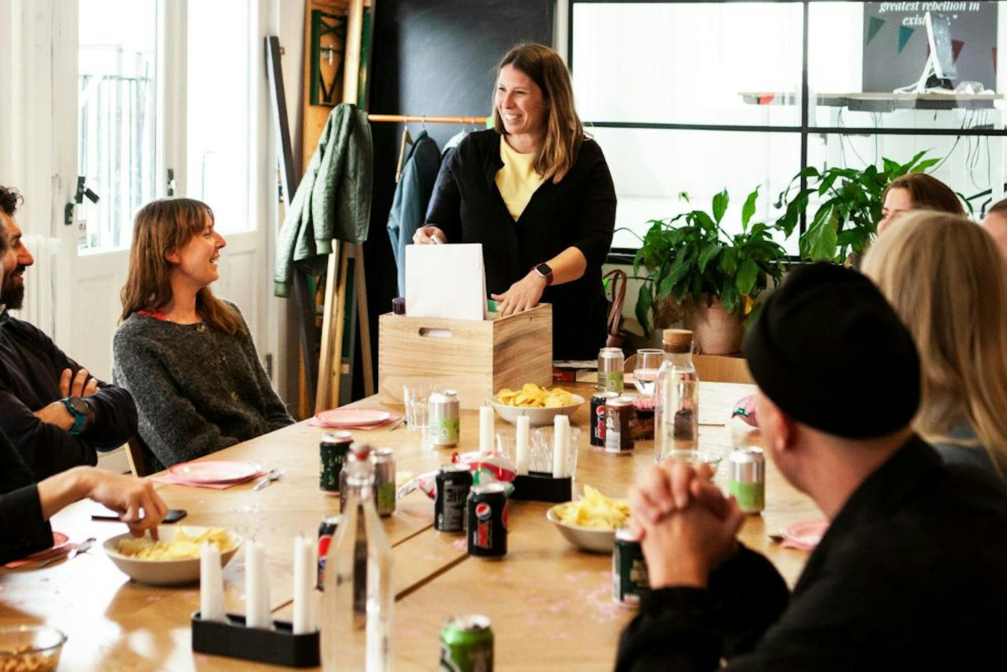 Team celebrating a promotion in a relaxed environment, with participants smiling, chatting, and interacting around a table with snacks and drinks