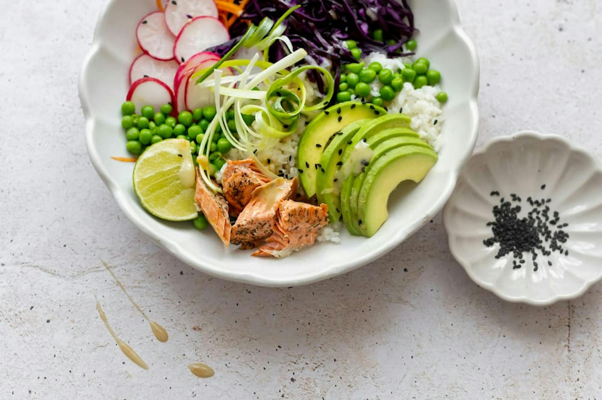 A colorful and healthy dish with rice, grilled salmon, avocado, peas, and sliced vegetables