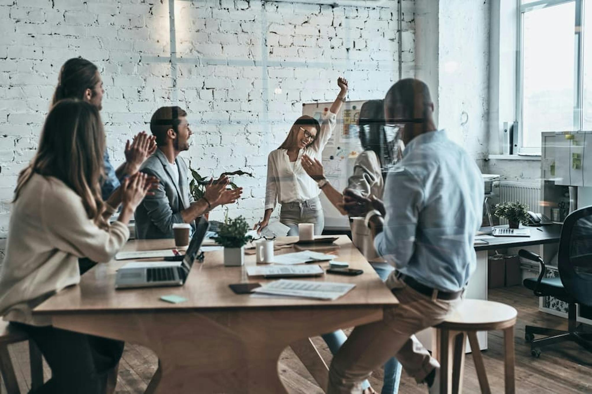 A work team is celebrating an achievement in a relaxed meeting. People are clapping and smiling