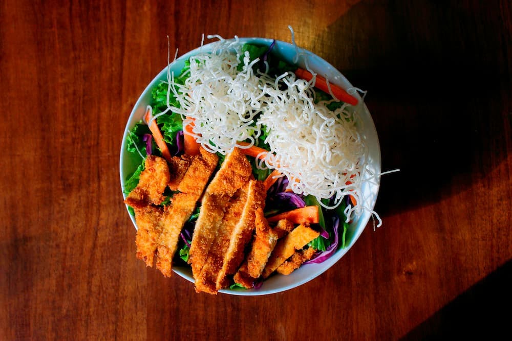 Colorful dish with breaded chicken fillet, fresh salad, and noodles on top