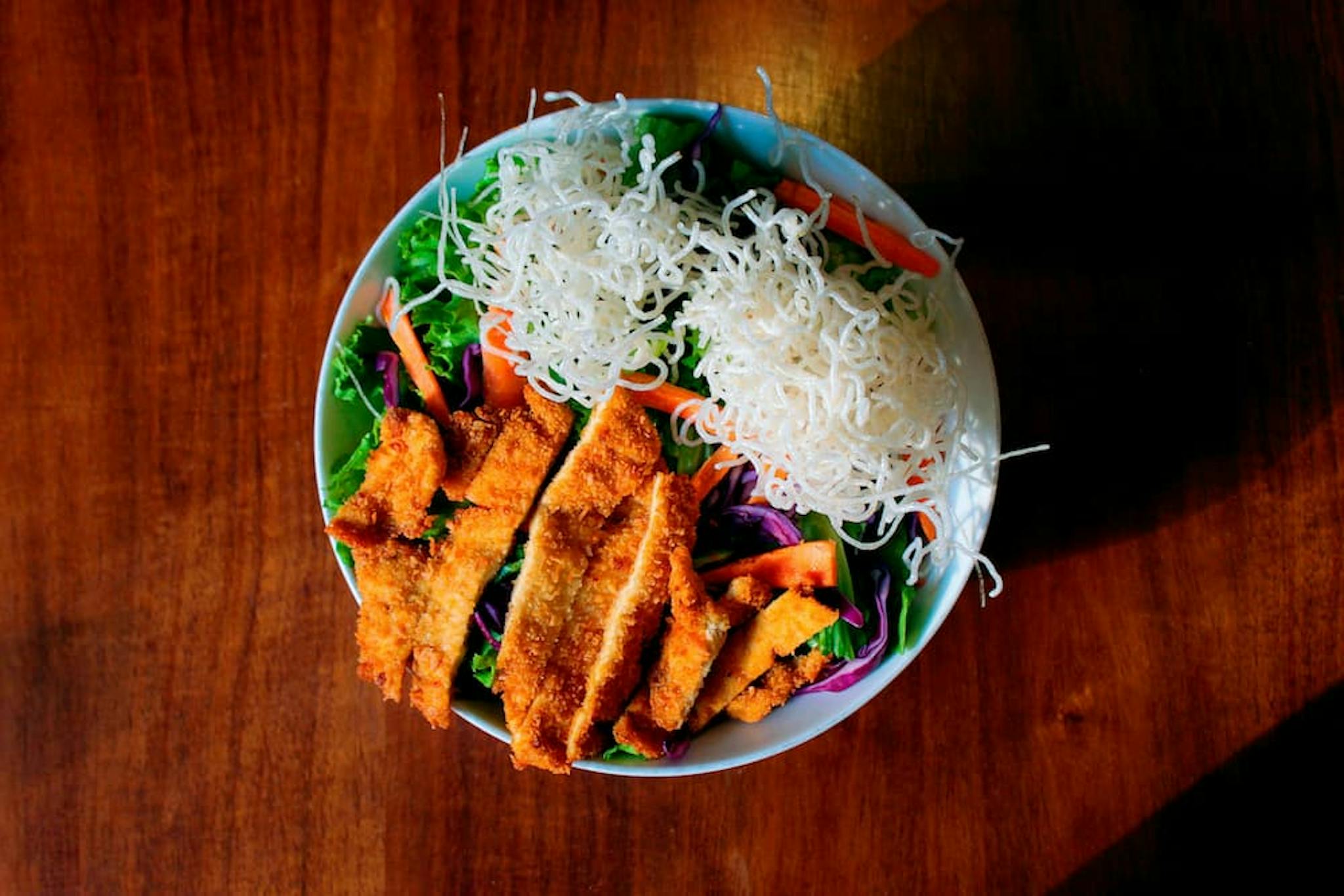 Colorful dish with breaded chicken fillet, fresh salad, and noodles on top