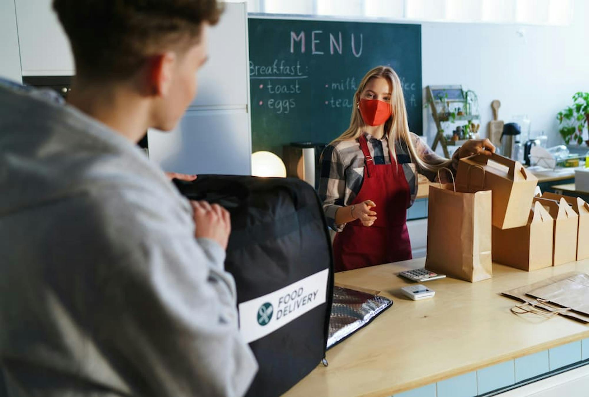 Food delivery attendant preparing orders in a modern kitchen, with focus on the interaction between the attendant and the delivery person