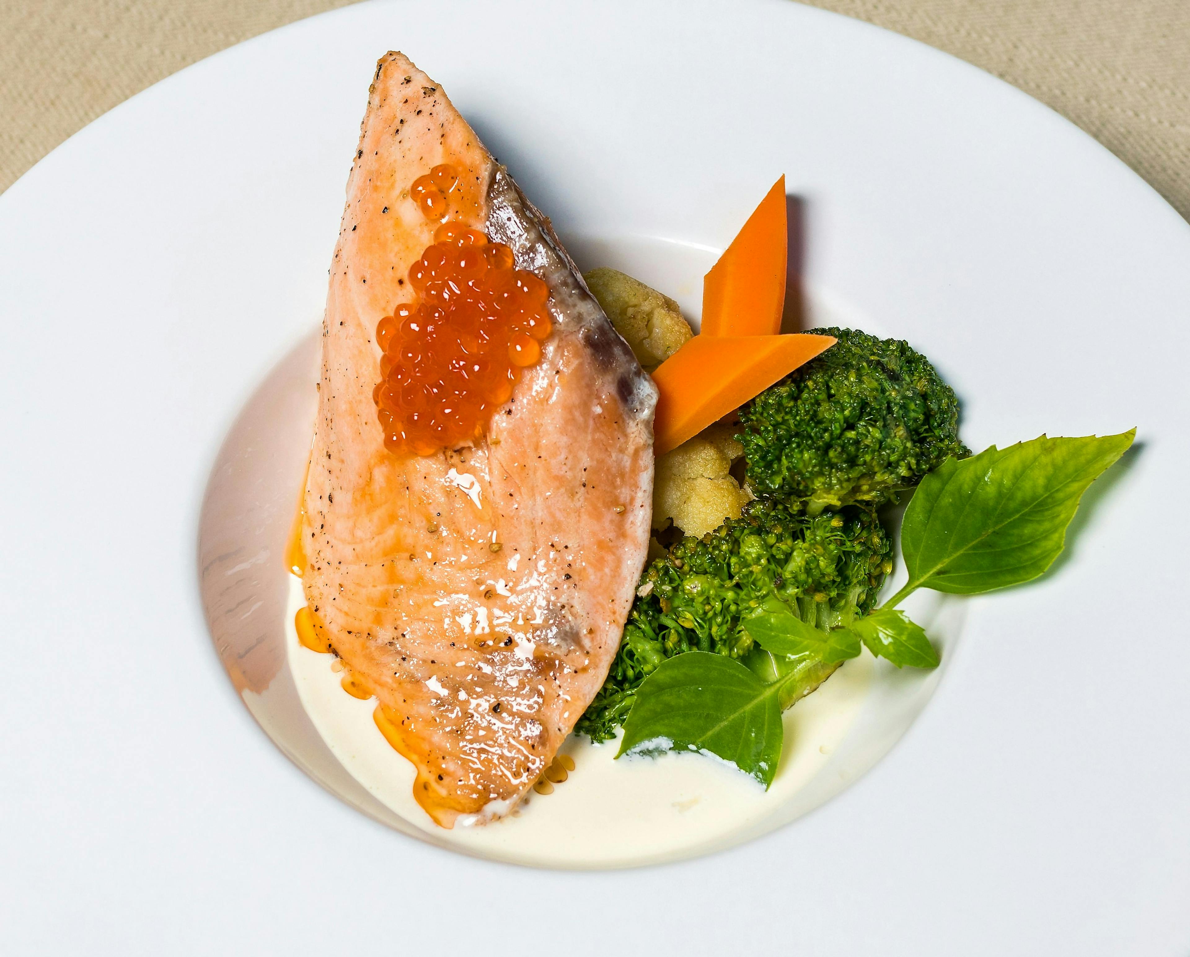 Grilled salmon dish with creamy sauce, broccoli, carrot, and fresh herbs