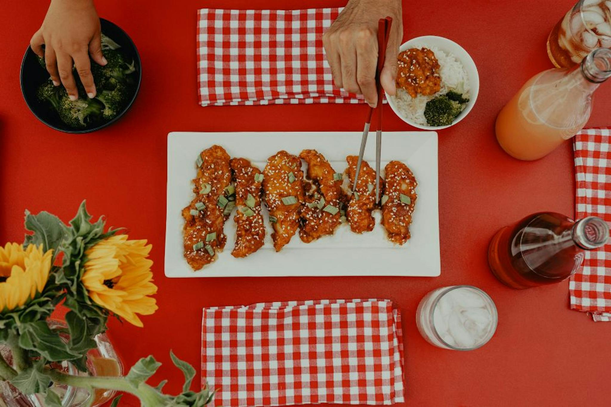 Dish featuring fried chicken covered in sauce, sesame seeds, and accompanied by rice and broccoli, with a decorated table