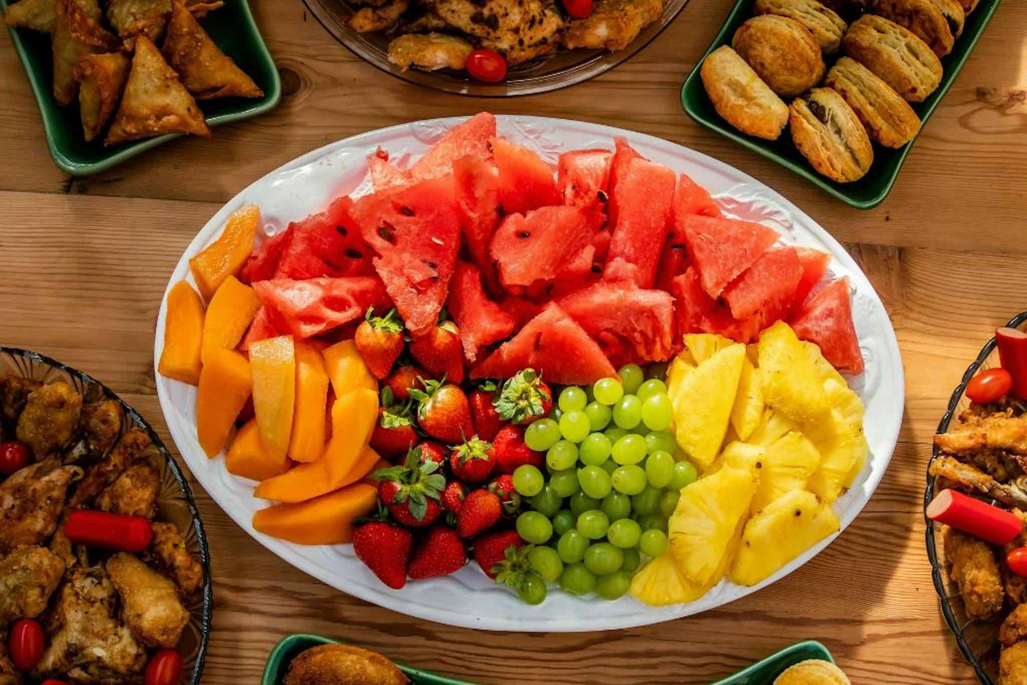 A beautiful tray of fresh fruits, including watermelon, pineapple, green grapes, strawberries, and papaya