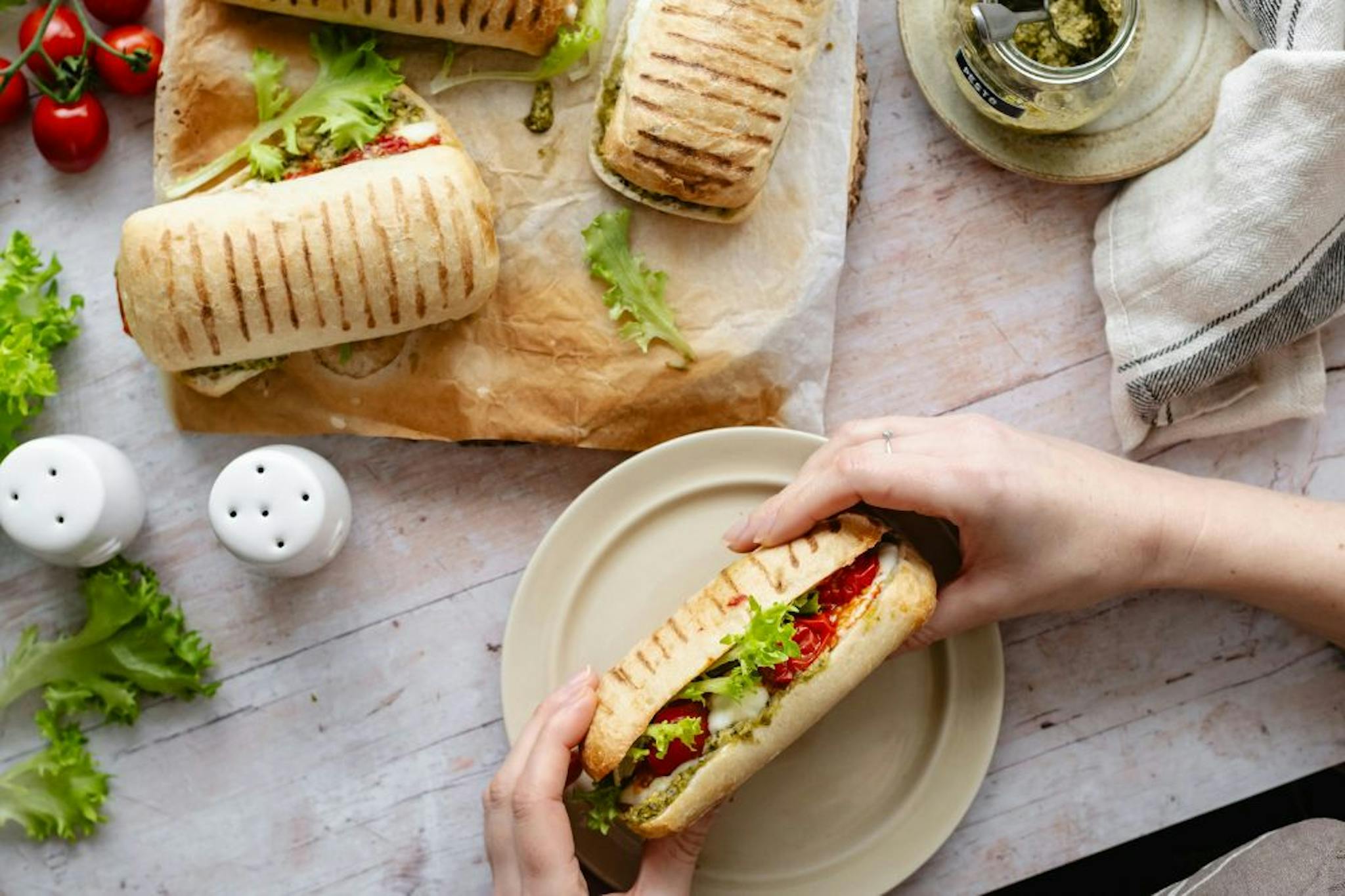 Delicious grilled sandwiches with fresh vegetables, served on a plate, accompanied by seasonings and fresh ingredients