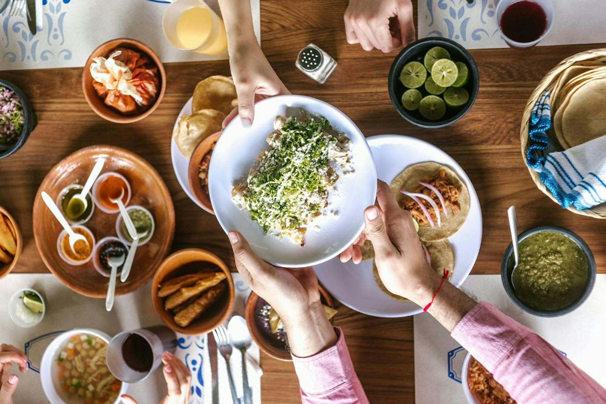 Shared meal with a variety of dishes, such as tacos, guacamole, and a main dish covered with cheese and herbs