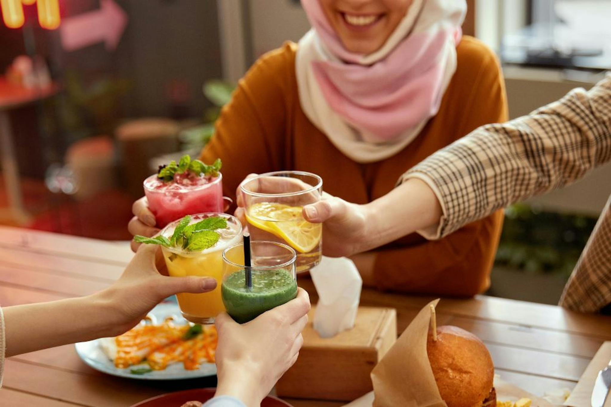 Group of friends toasting with colorful drinks at a table full of delicious dishes