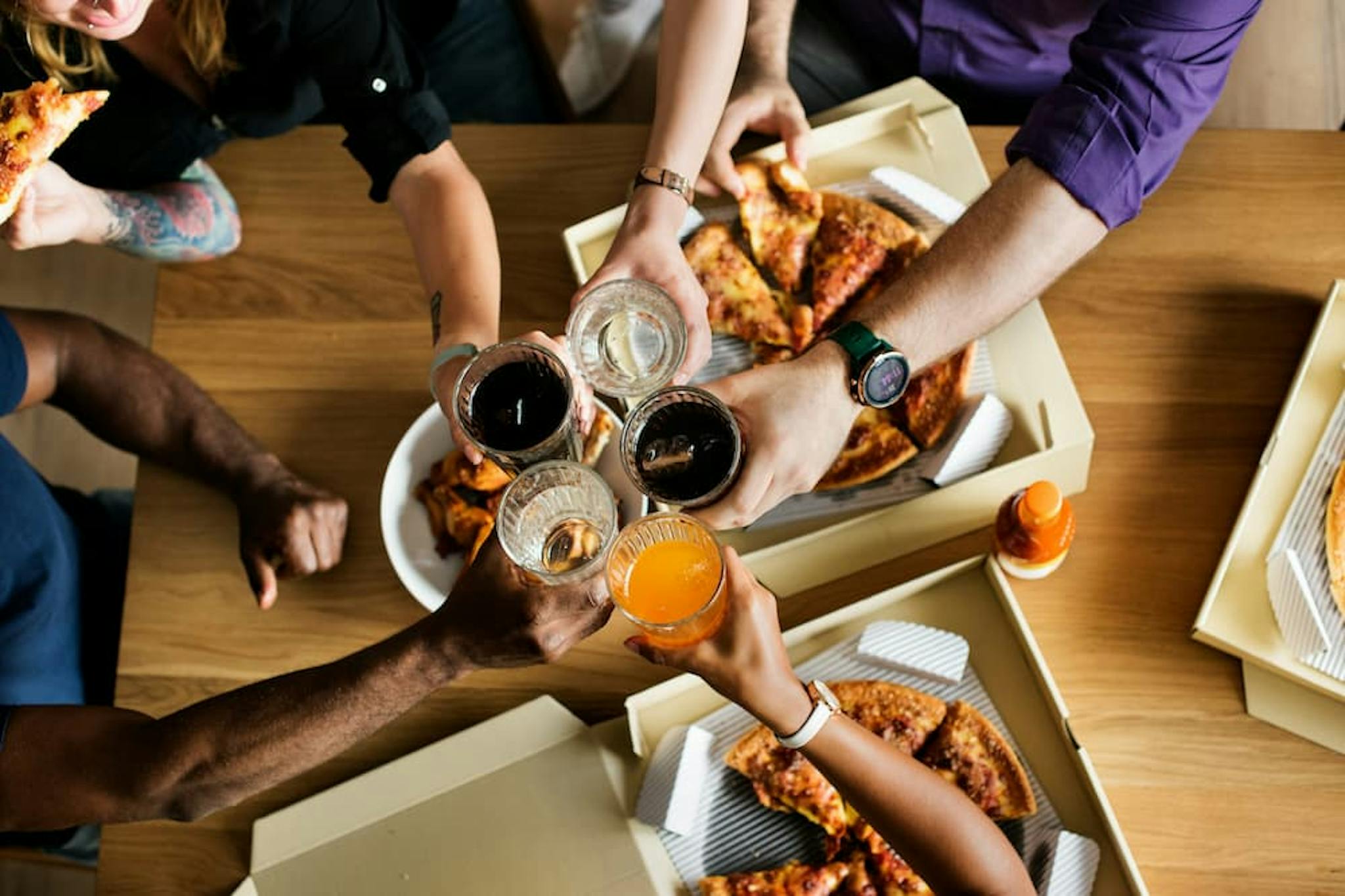 A group of friends gathers around a table to share pizzas and cheerful toasts.