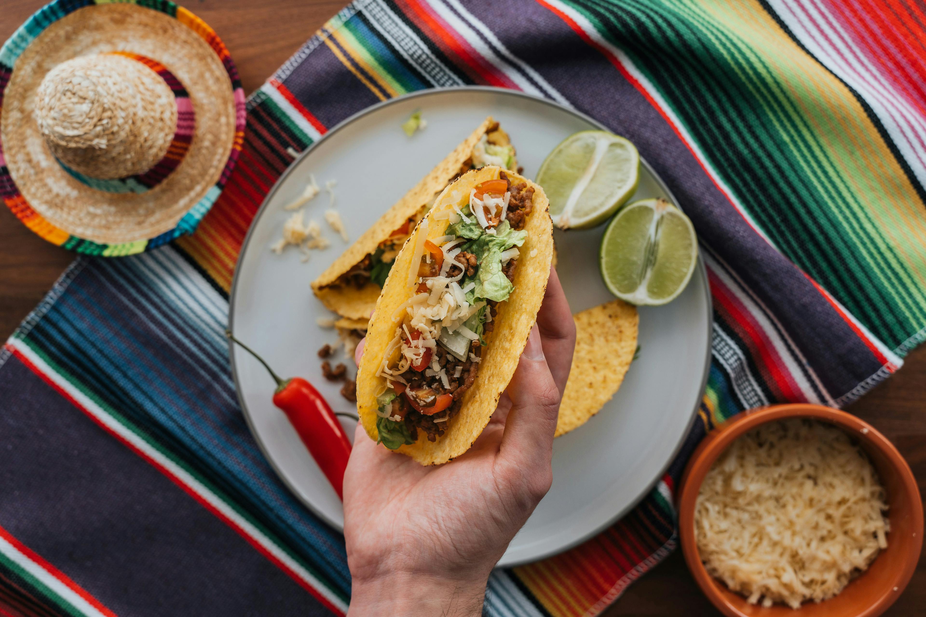 Delicious taco filled with meat, salad, and cheese, accompanied by limes and rice, in a festive setting with a colorful tablecloth