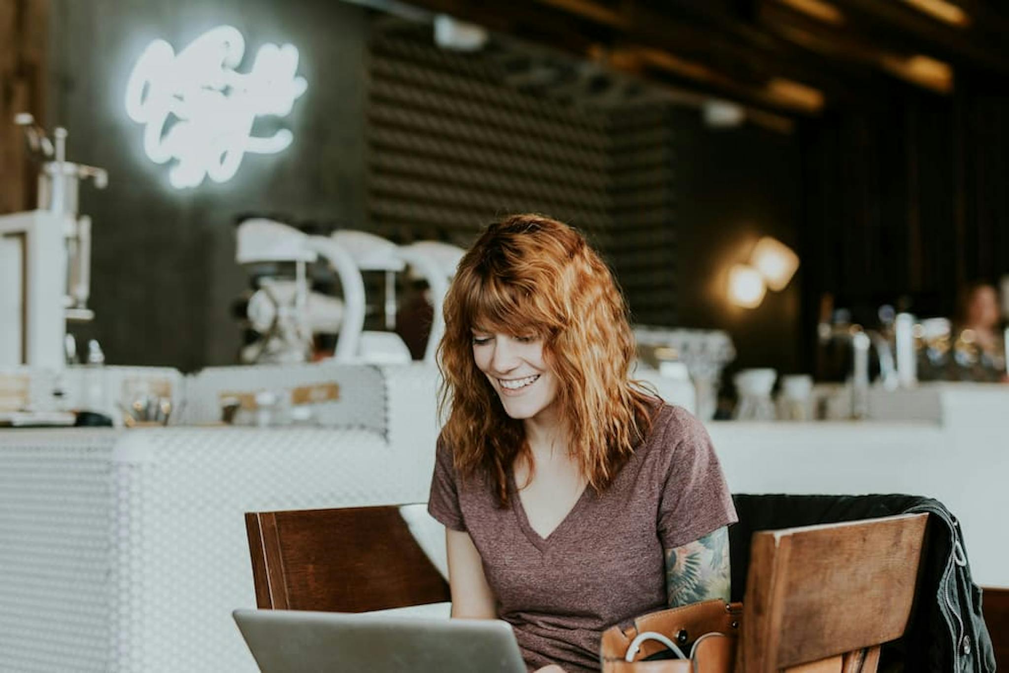 Smiling woman using a laptop in a breakroom, with a cozy atmosphere and coffee equipment in the background.