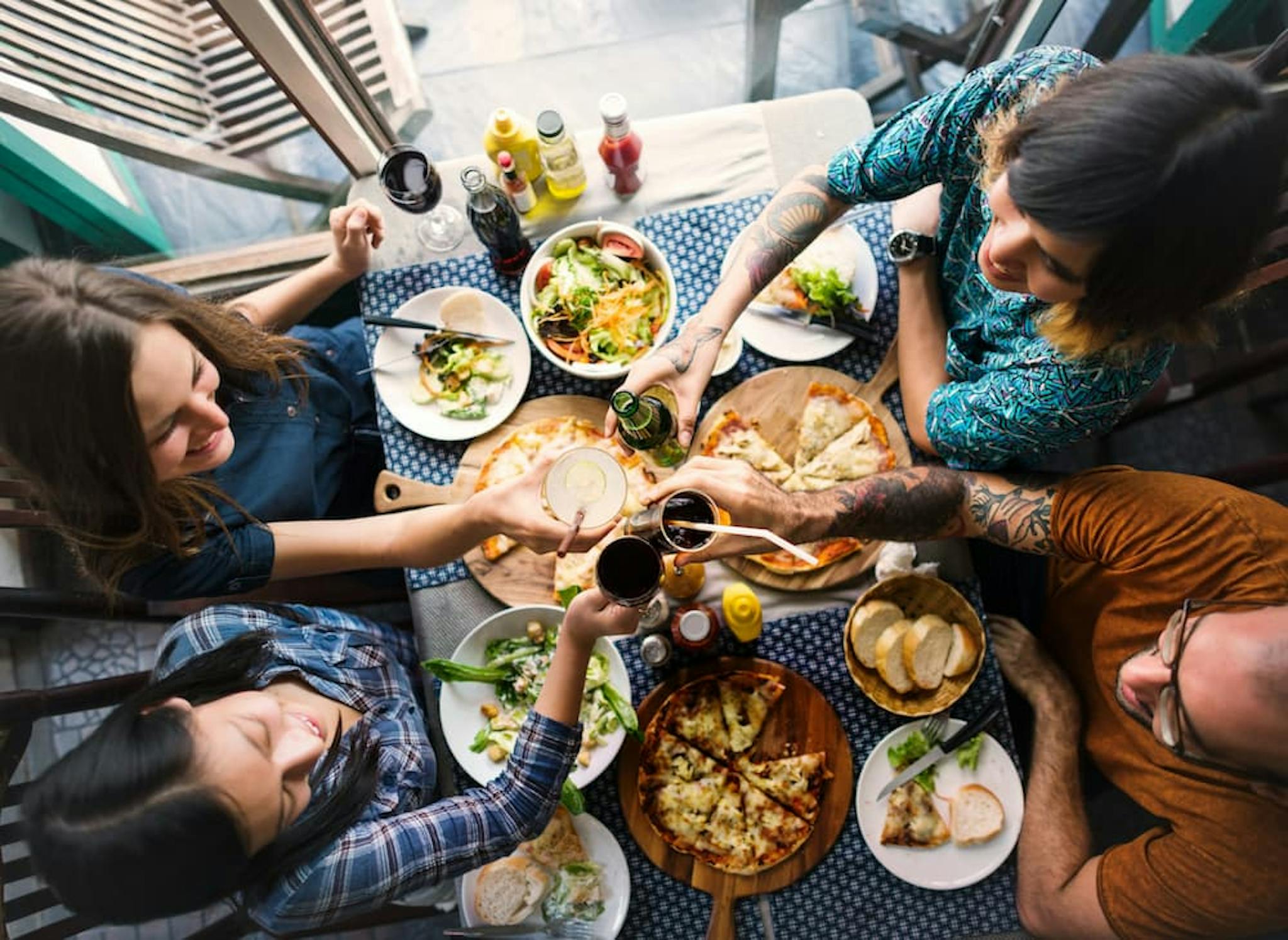 A group toasting over a table full of various foods, including salads, pizzas, and drinks.