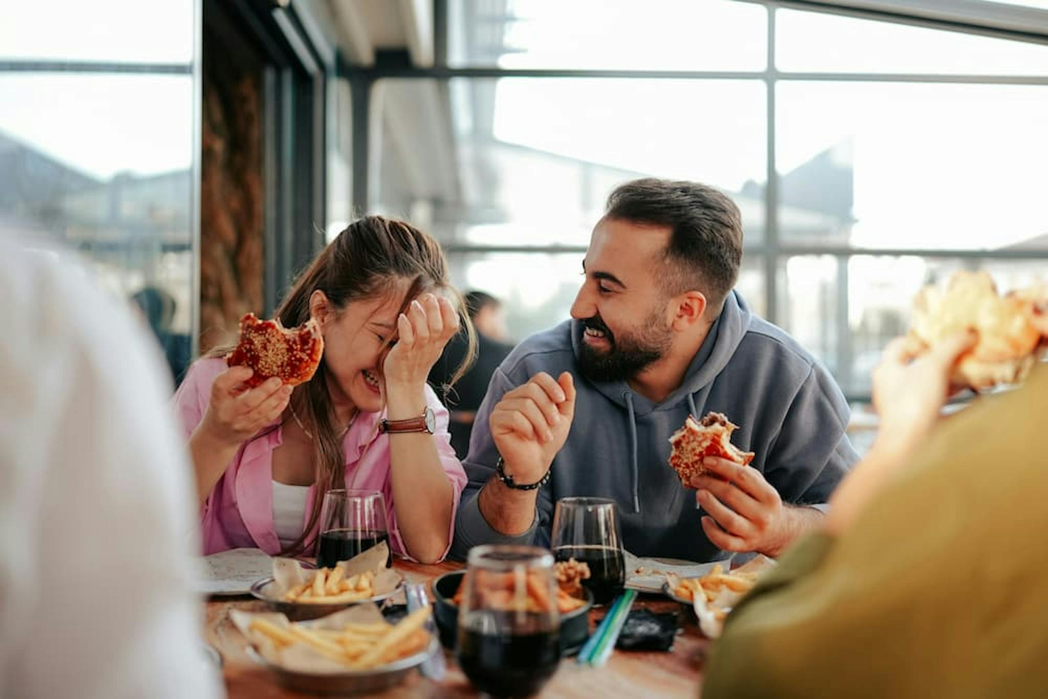 A couple having fun during a meal, eating hamburgers and fries, in a relaxed and cheerful environment.