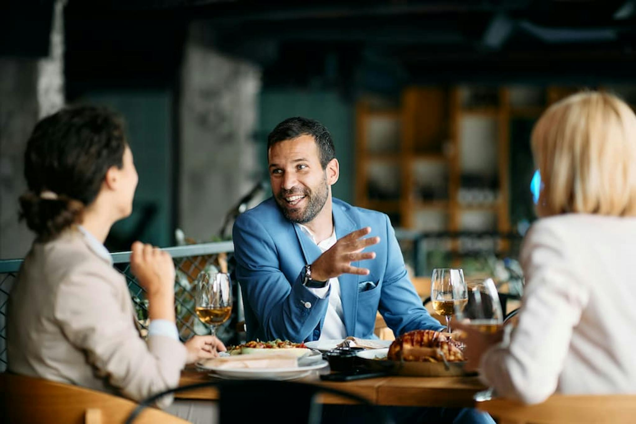 Group of professionals chatting in a modern restaurant, enjoying a relaxed moment with food and drink. Smiles and interaction highlighted.