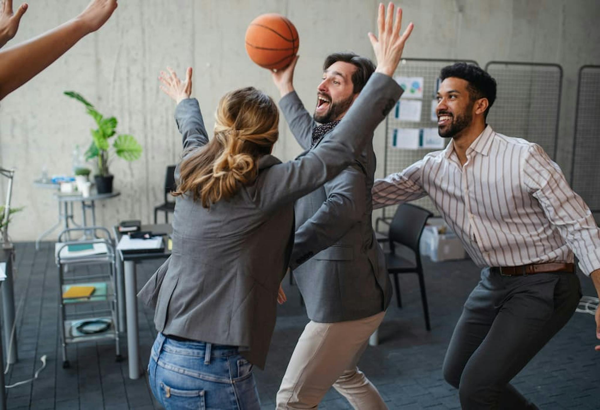 A group of professionals having fun in a work environment by playing basketball, promoting the importance of leisure and teamwork.