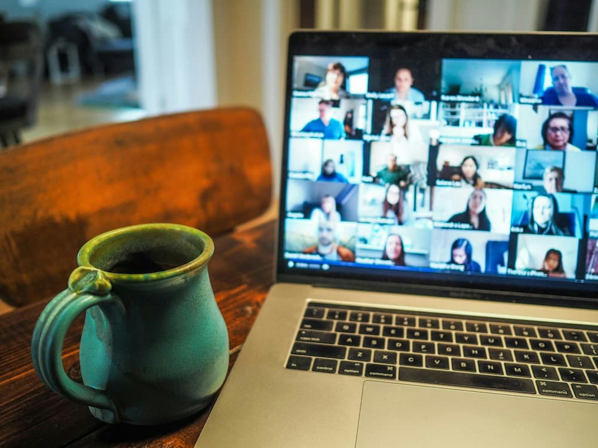 Virtual remote work meeting with several people on a video call, accompanied by a coffee mug on a wooden table.