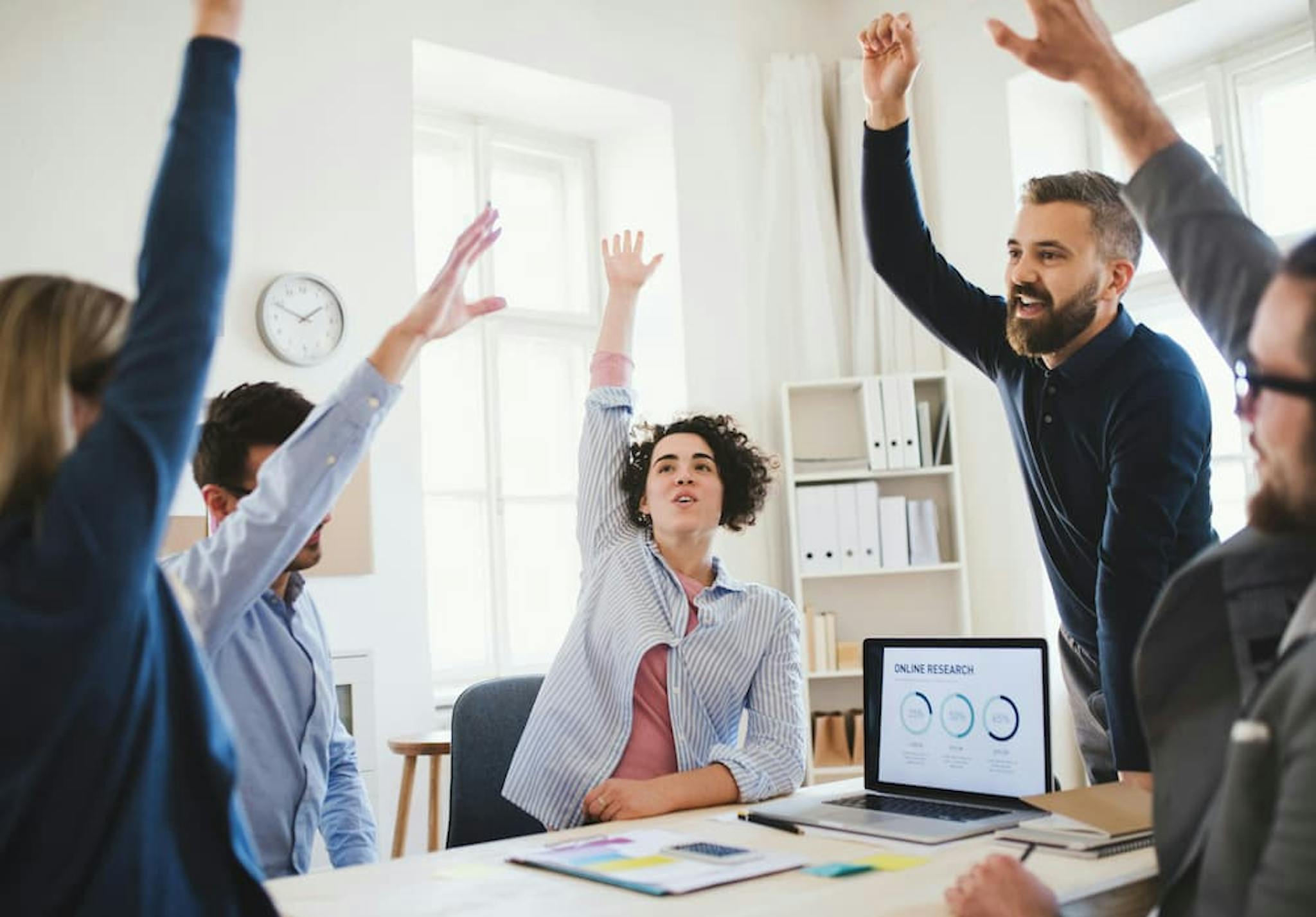 Team meeting in a modern office, with employees raising their hands during a discussion.