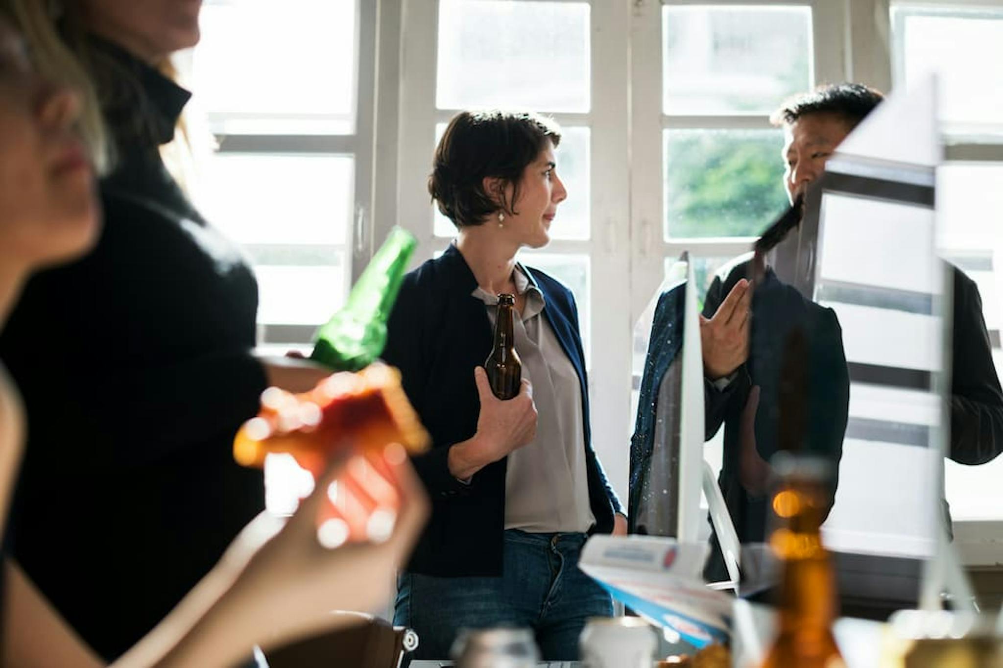 Group of people in an office, talking and holding drinks.