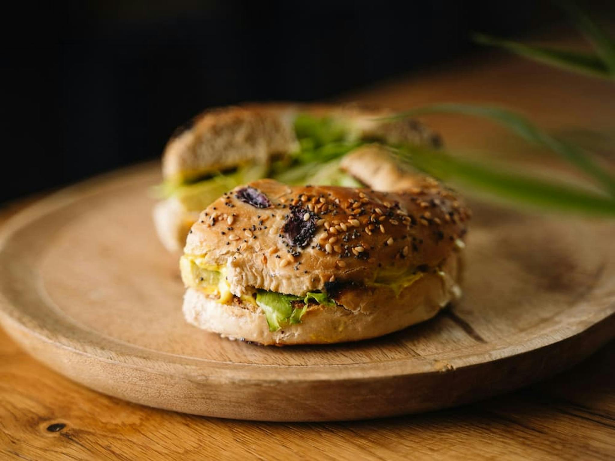 Bagel sandwich with sesame seeds, filled with fresh ingredients, served on a wooden plate