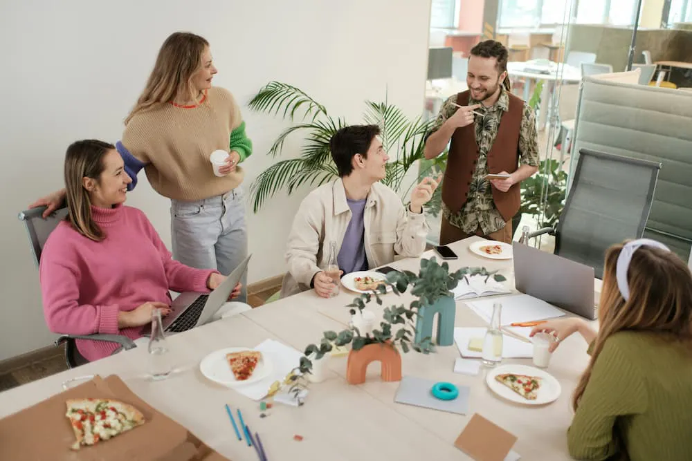 Group of people in a casual meeting, enjoying pizza, with a modern office environment