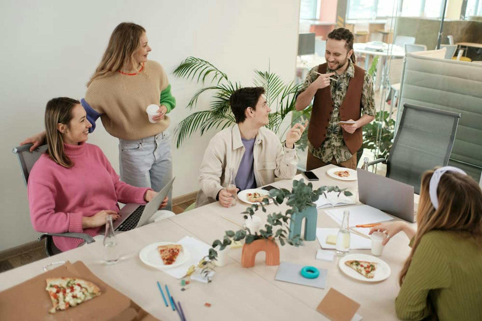 Group of people in a casual meeting, enjoying pizza, with a modern office environment