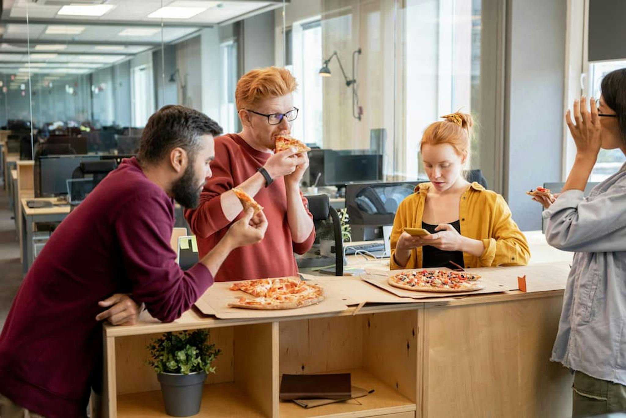 Group of colleagues enjoying pizza in an office, with computers in the background