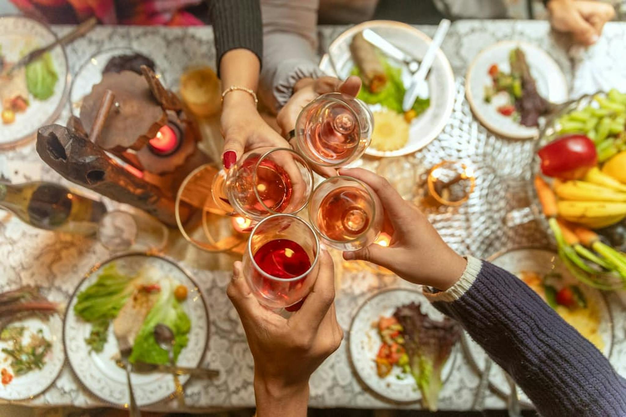 People making a toast at a table with various dishes and a basket of fruit in the background, symbolizing unity and celebration