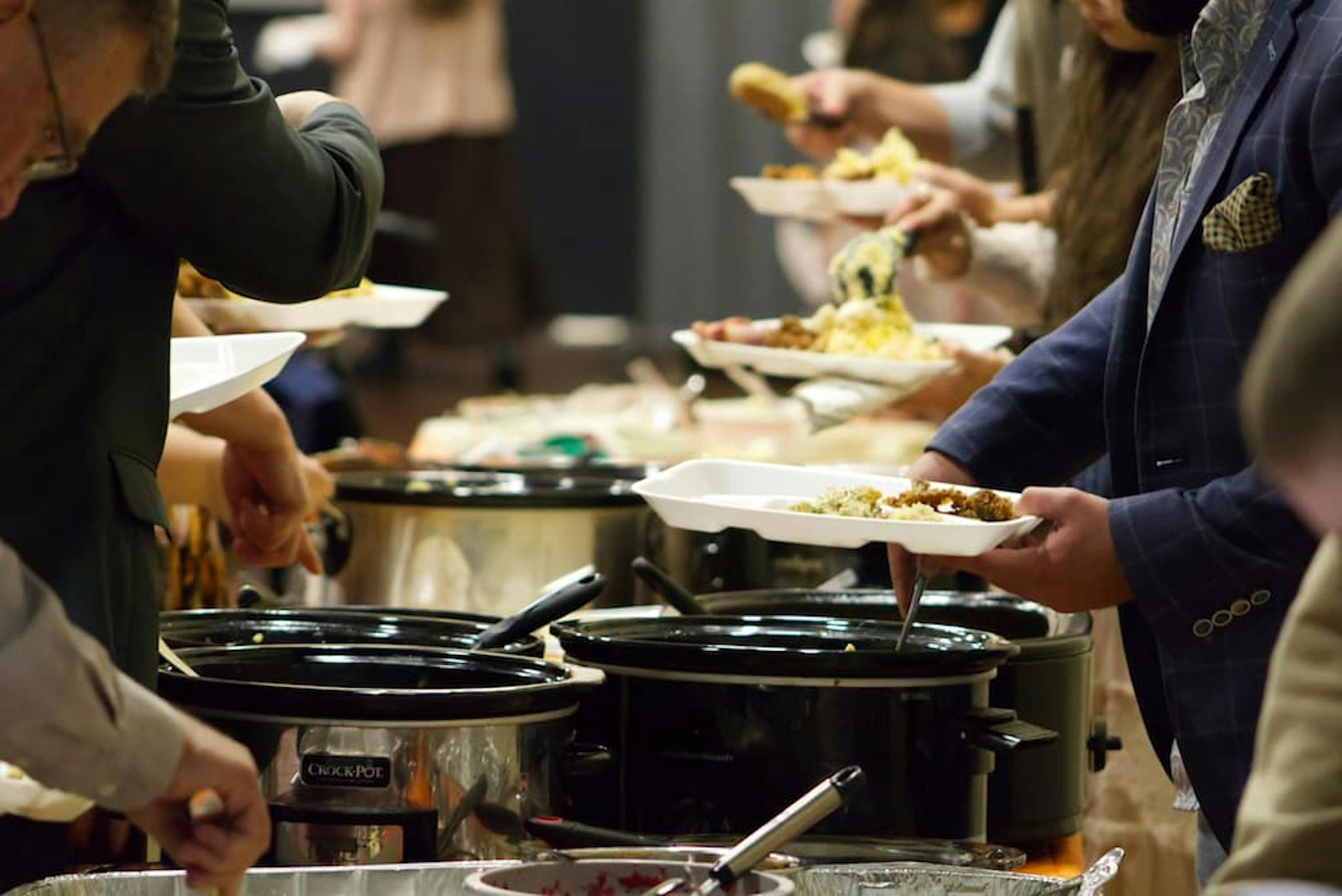 Lunch buffet with several people serving food. The plates are full, and there are large pots with different dish options.