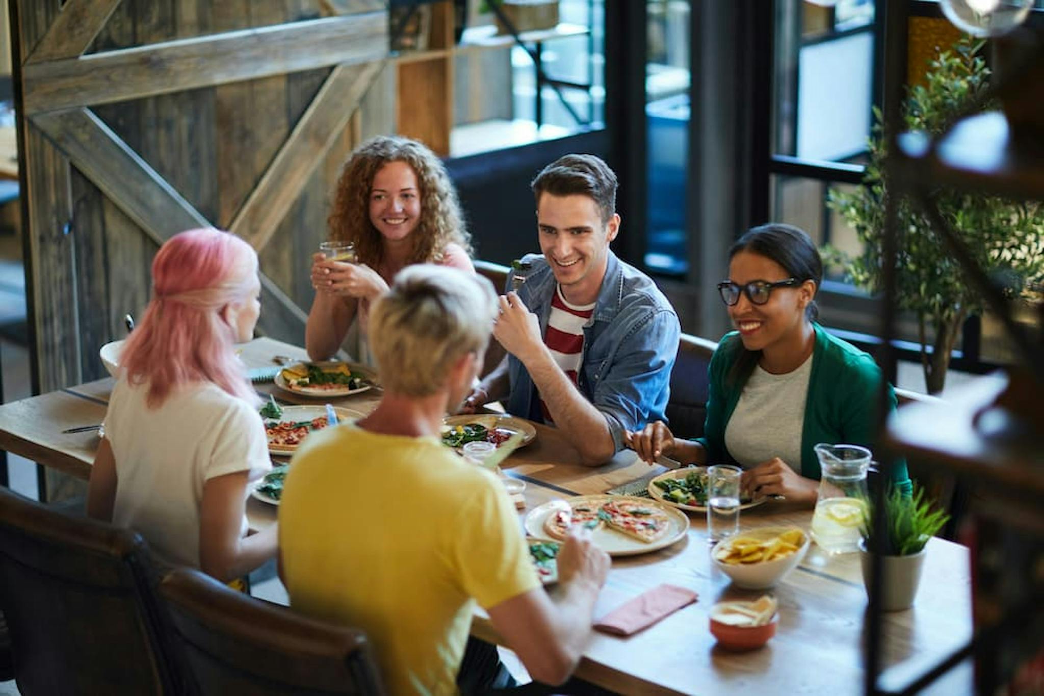 A group of colleagues having fun at a casual lunch in a restaurant, with various dishes on the table, smiles, and toasts