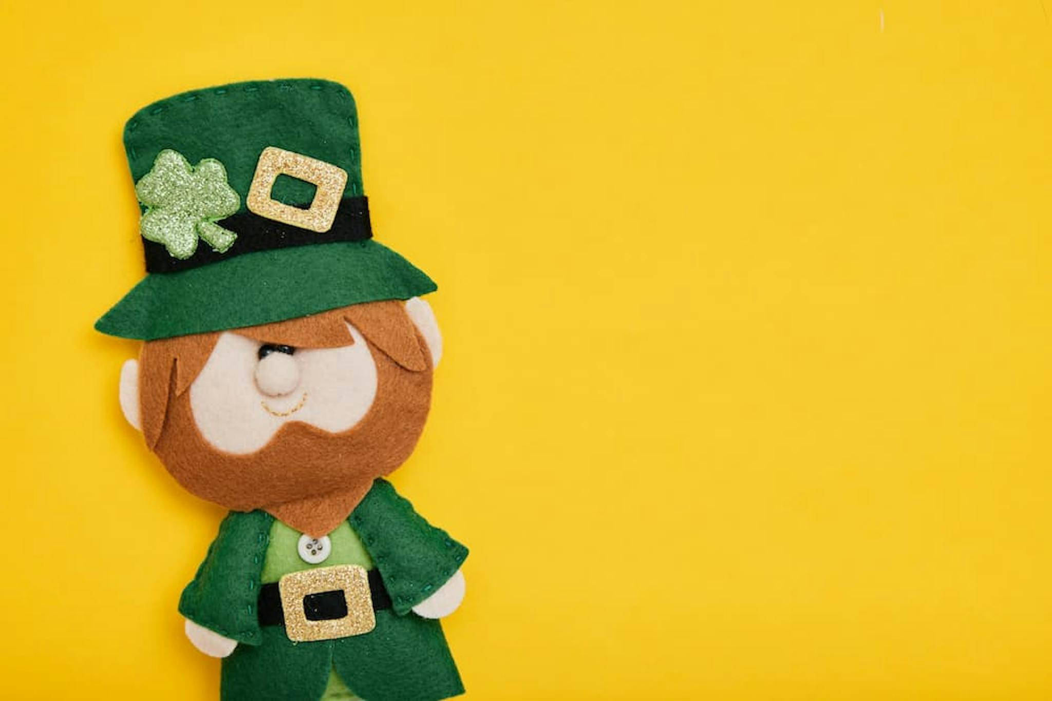 Felt leprechaun doll with a green hat and shamrock, highlighted against a yellow background.