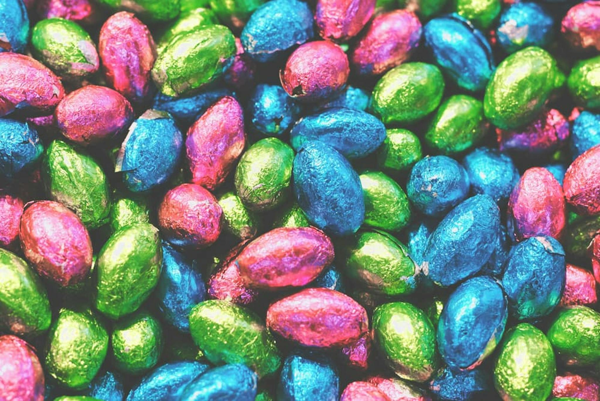 Chocolate eggs wrapped in metallic paper, in green, blue, and pink colors.