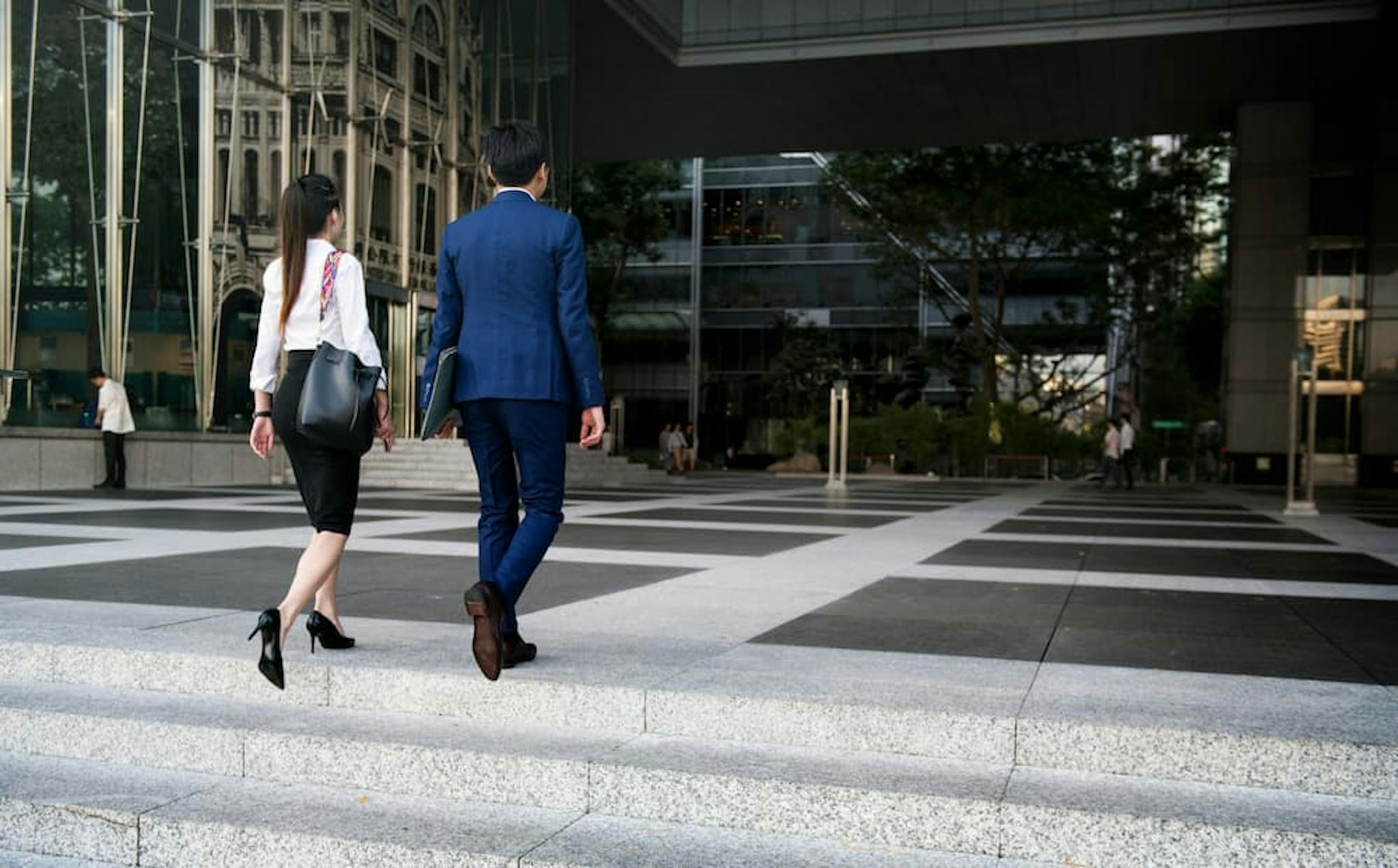 Two business professionals, one in a blue suit and the other in a white blouse and black skirt, leaving the office.