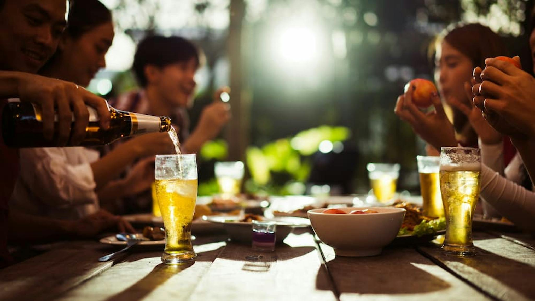 A group of colleagues gathered around a wooden table outdoors, enjoying drinks and food during a happy hour.