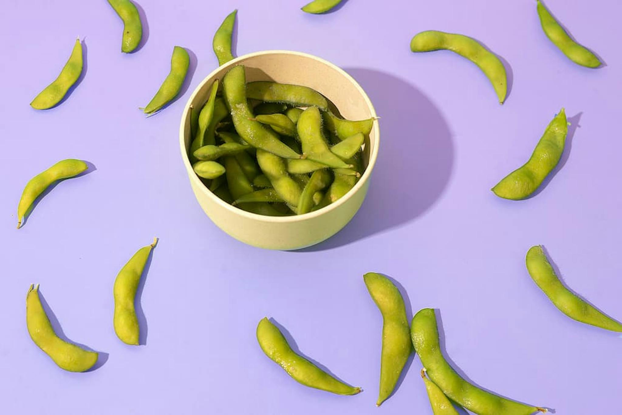 A bowl filled with green edamame pods is placed on a purple surface.